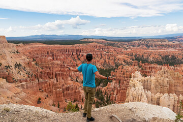 Naklejka premium Rear view of man spreading his arms with aerial view of massive hoodoo sandstone rock formations, Bryce Canyon National Park, Utah, USA. Natural amphitheatre sculpted red rocks of Claron Formation