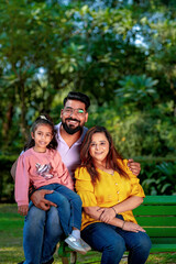 Happy Young indian parents with their cute little daughter sitting at park or garden.