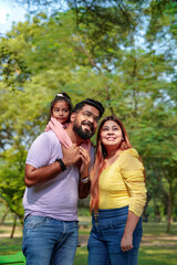 Naklejka premium Happy Young indian parents with their cute little daughter sitting at park or garden.