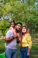 Happy Young indian parents with their cute little daughter sitting at park or garden.