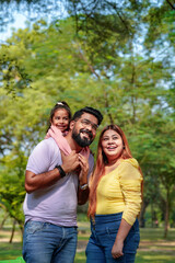 Happy Young indian parents with their cute little daughter sitting at park or garden.