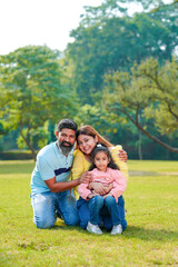 Fototapeta premium Happy Young indian parents with their cute little daughter sitting at park or garden.