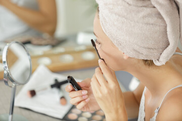 Obraz na płótnie Canvas pretty young woman with towel on head applying mascara