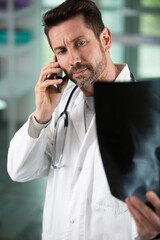 doctor with smartphone looking at x-ray in office