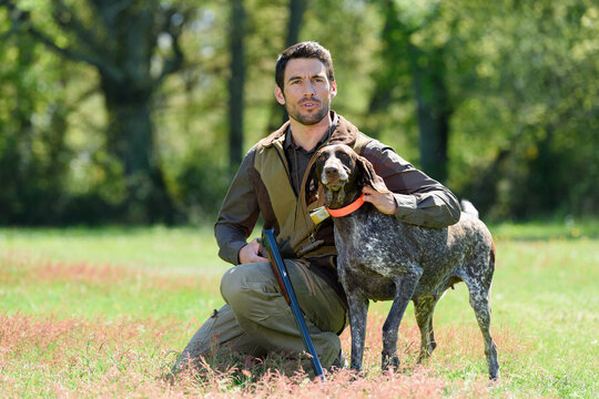 male hunter with gun crouched beside his dog
