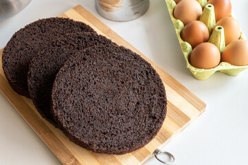 Chocolate brown biscuit round cake layers lie on the kitchen table, chicken eggs in the tray