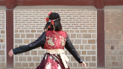 Young woman in korean national costume hanbok is spinning against the background of an ancient wall.