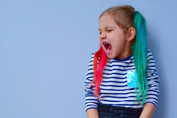 The child is a rebel. A little girl with colored hair and crossed arms on her chest against a gray background stubbornly turns aside, not wanting to listen to anyone. Parenting problems, naughty child