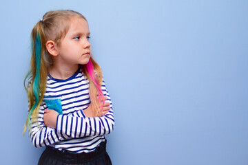 The child is a rebel. A little girl with colored hair and crossed arms on her chest against a gray background stubbornly turns aside, not wanting to listen to anyone. Parenting problems, naughty child