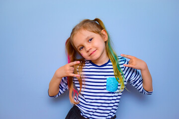 A pretty girl with hair dyed in different colors, one tail pink, the other green, stands on a blue background. Rebel child, cheerful modern fashionable schoolgirl. Generation Z.