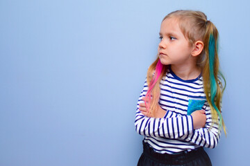 The child is a rebel. A little girl with colored hair and crossed arms on her chest against a gray background stubbornly turns aside, not wanting to listen to anyone. Parenting problems, naughty child
