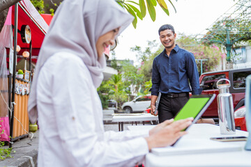 Fototapeta na wymiar Asian businessman comes on foot as veiled woman sits using digital tablet at coffee shop