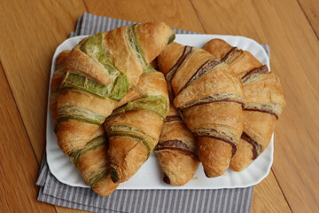Many sweet chocolate and pistacchio croissants on a white ceramic tray on wooden table