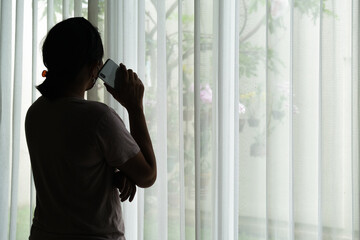 Silhouette of a woman who is standing by the window making a phone call.