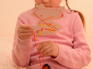 The child learns to embroider with a cross. A cute little girl with pigtails learns to cross-stitch...