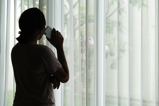 Silhouette of a woman who is standing by the window making a phone call.