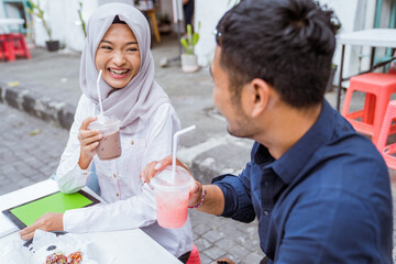 young Asian couple sits laughing and enjoying drinks together at a coffee shop