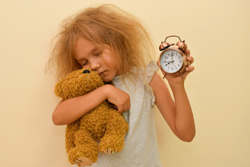 A sleepy child yawns with an alarm clock in his hands. Early rise to school or kindergarten. The...