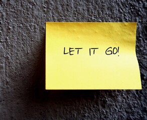 A yellow note pad on the grey rough textured cement wall, with a message LET IT GO to remind...
