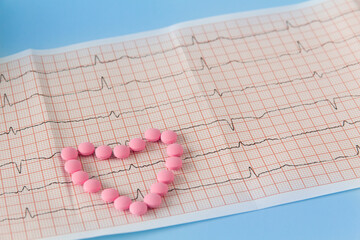 A large handful of pink pills lie in the form of a heart on an electrocardiogram, on a blue...