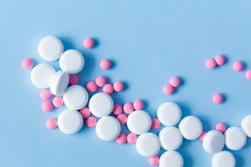 A large handful of white, round pills and pink medicines against a blue background. The concept of a healthy lifestyle and timely medical examination.