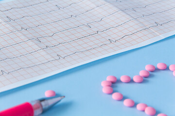 A large handful of pink pills lie in the form of a heart on an electrocardiogram, on a blue background. The concept of a healthy lifestyle and timely medical examination.