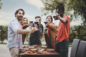 Friends Toasting with Red Wine - Mixed-age group, including two men and a woman in their 40s, a young plus-size person, and a 25-year-old African person, toasting wine glasses, looking at the camera.