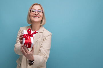 middle-aged business concept. a woman in a jacket holds a gift box with a bow on a studio background with copy space