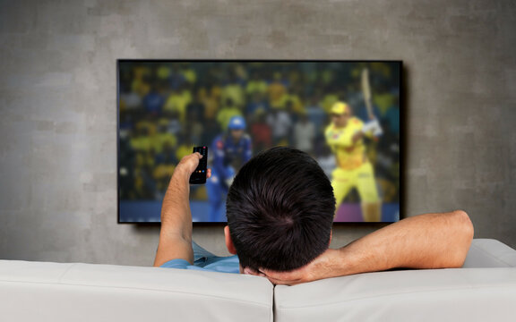 Rear view of a man sitting at home watching cricket matches on TV: sports, competition, entertainment, and technology concept digital composite image.