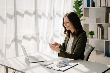 Confident business expert attractive smiling young woman typing laptop ang holding digital tablet  on desk in creative home office.