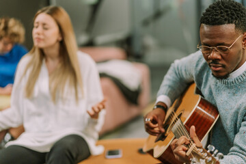 A close up photo of handsome black male playing guitar. His white blonde female colleague is singing