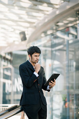 Fototapeta premium Handsome unshaven businessman walking with tablet and smartphoneon city street.