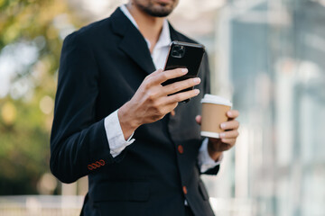 Professional businessman using smartphone and holding coffee to go while working at office.