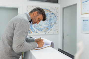 Writing down the information. Dentists patient filling up her medical application form standing with the doctor at reception.