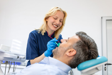 Female dentist treating teeth to patient, mid age man in chair at dental clinic. Dentistry, healthy teeth, medicine and healthcare concept