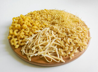 Pasta of different types on a round wooden stand on a white background