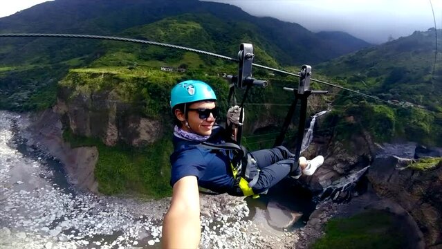 Young man rides zipline by green mountains in Ecuador, selfie shot