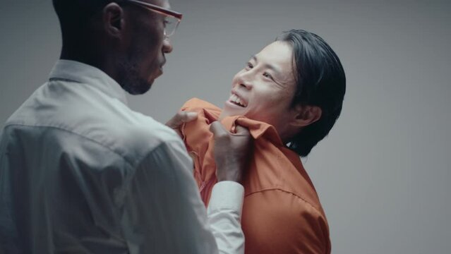Aggressive black cop beating a confession out of mad Asian gangster, holding him tight, using physical force and threatening during interrogation