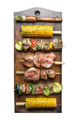 Isolated of various raw meat skewers with vegetables and corn with green herbs sauce on wooden...