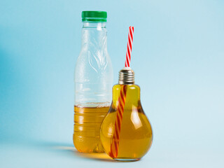 Half empty plastic bottle with drink and juice in glass reusable bottle on blue background. Concept of earth day, zero waste and plastic recycling.