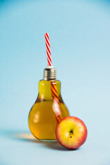 Apple drink juice in a reusable glass bottle with a straw on a blue background. Concept of earth day, zero waste and plastic recycling.