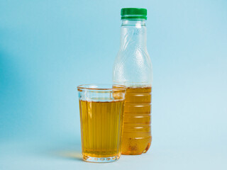 Glass of juice and plastic bottle on blue paper background. Concept of earth day, zero waste and plastic recycling.