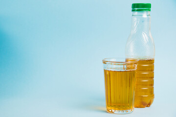 Glass of juice and plastic bottle on blue paper background. Concept of earth day, zero waste and plastic recycling.