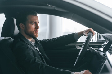 Serious facial expression. Driving the car. Man in formal business clothes is sitting in the modern automobile