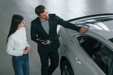 Fototapeta premium Top view. Man is showing the new automobile to the woman customer in the car dealership