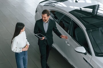 Fototapeta premium Top view. Man is showing the new automobile to the woman customer in the car dealership