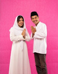 portrait of Asian man and woman with salam in Muslim clothes with pink background