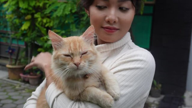 A beautiful Asian woman is carrying her orange Angora cat