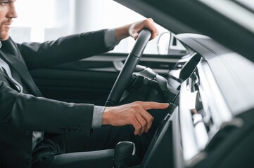 Turning the knobs. Man in formal business clothes is sitting in the modern automobile