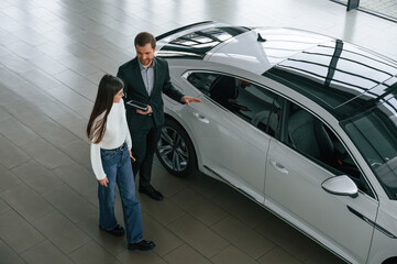Fototapeta na wymiar Talking, holding tablet. Man is showing the new automobile to the woman customer in the car dealership